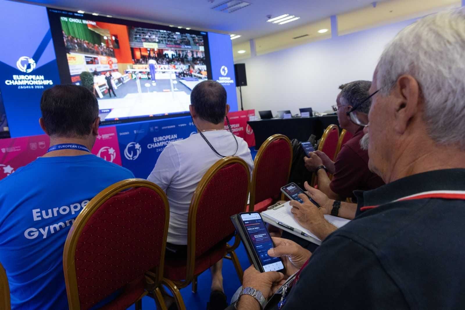 A routine playing on the arena's big LED screen while several judges score it on their phones in the Elevien Academy app.