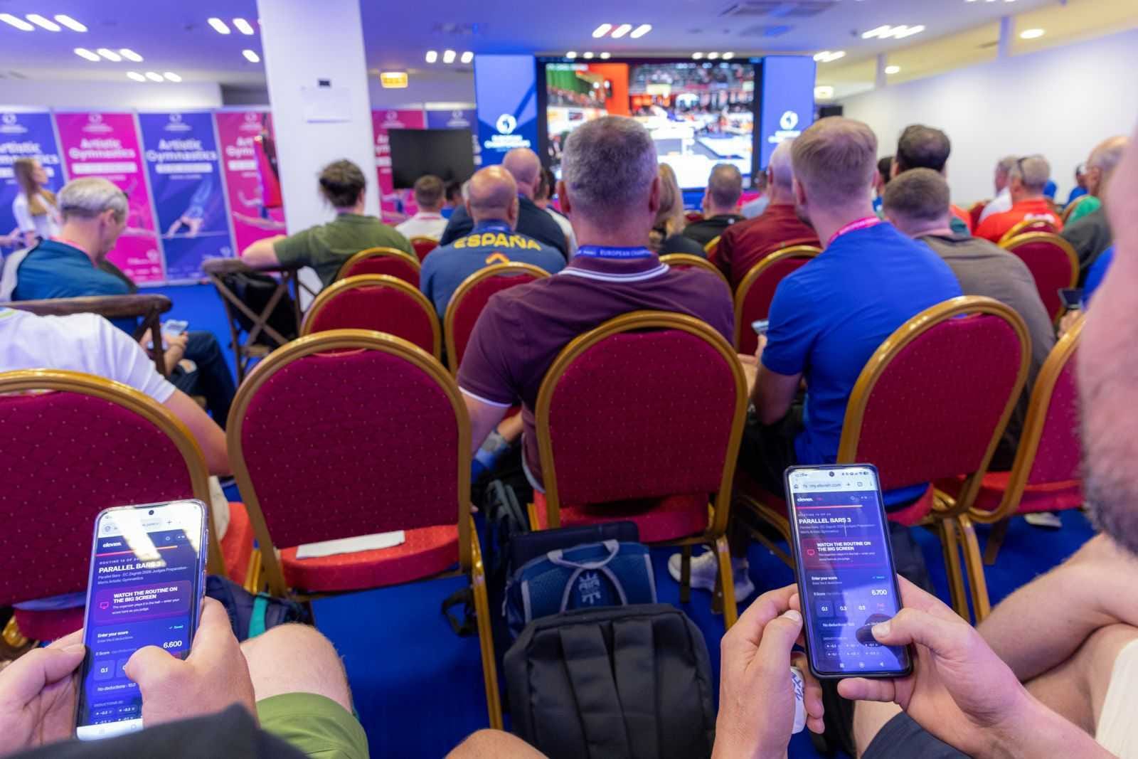 Two judges' phones running the exam side by side, with the hall and the big screen behind them.